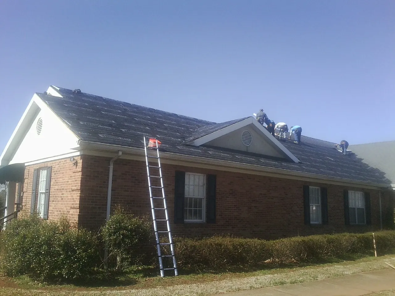 Crew tearing shingles off a brick ranch roof with a ladder set — Metal Roof Repair work by our crew in Mayo