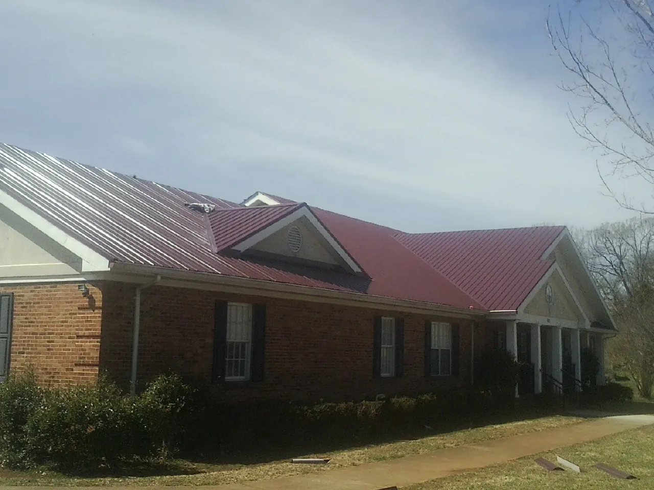 Red metal roof with gabled entries on a long brick building, from a Hail Damage Roof Repair job in Mayo