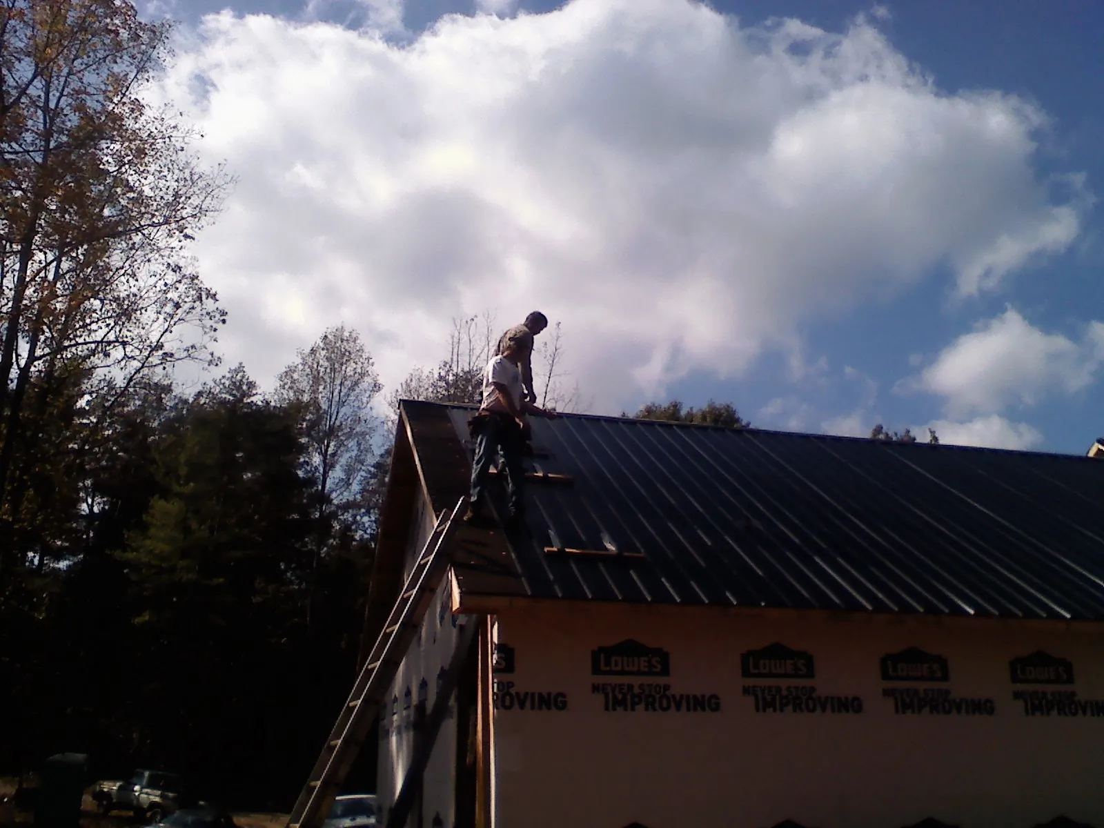 Roofer fastening dark metal panels high against a cloudy sky, from a Roof Inspection job in Mayo