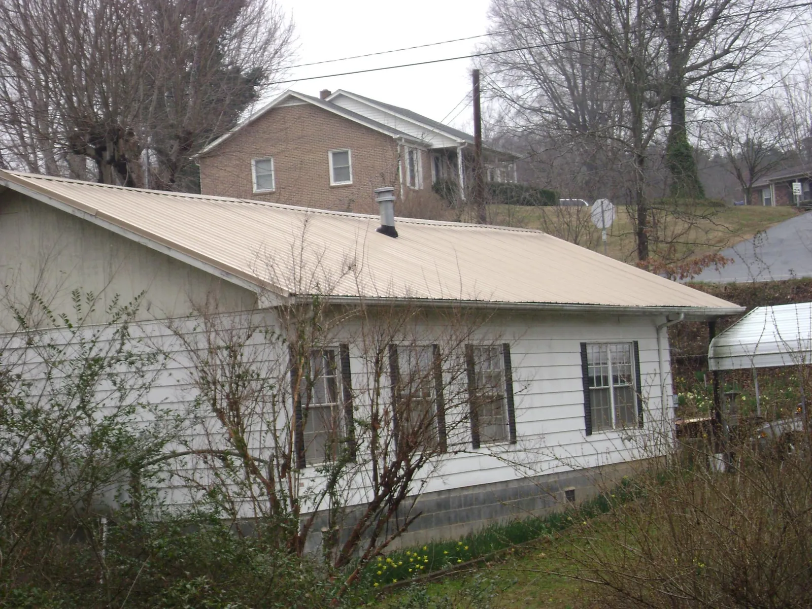 Tan metal roof on a white sided house set into a hillside — Commercial Roofing by Roofing Brothers in Mayo